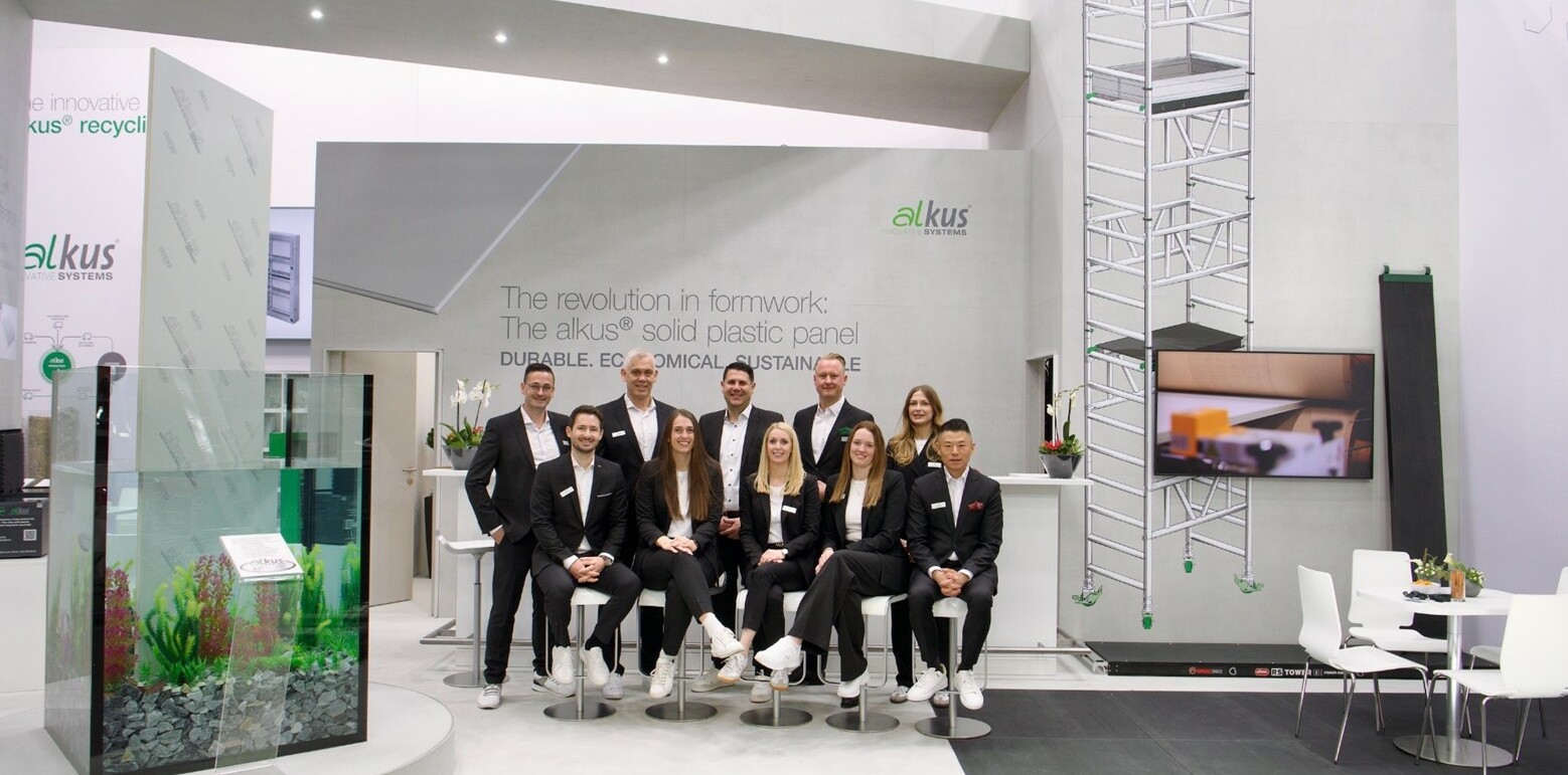 The alkus team with the new Managing Director Daniel Keller and owner Julian Dingler (2nd row, 3rd and 4th from left) in front of the alkus AG stand, with the aquarium on the left. | © alkus AG / Jens Ellensohn