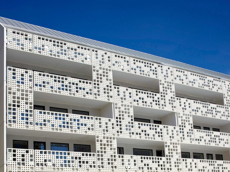 Die vorgelagerte Fassade aus strahlendem Weiß dient als raffinierter Sichtschutz und bietet durch die Perforierung eine hohe Transparenz.