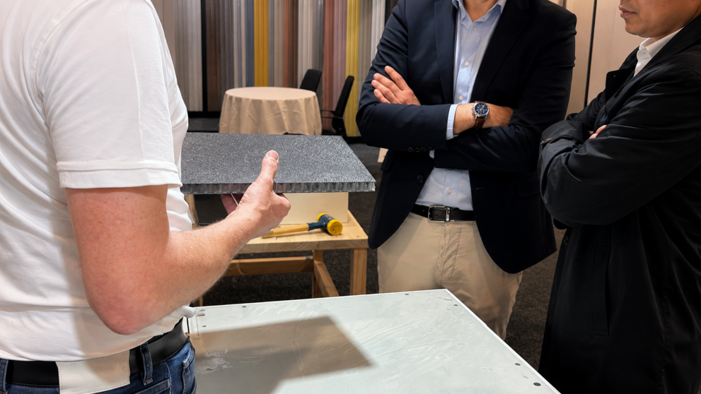 Business professionals reviewing a Comfodeck powered by alkus lightweight polypropylene panel during a product demonstration at an indoor trade show booth.